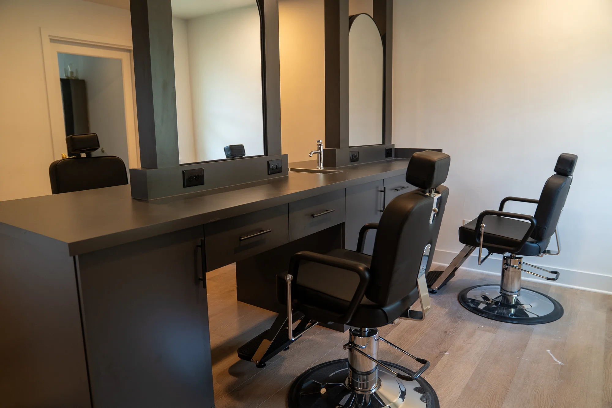 Black barber chairs facing arched mirrors and gray workstations at Paramount Barber Academy.