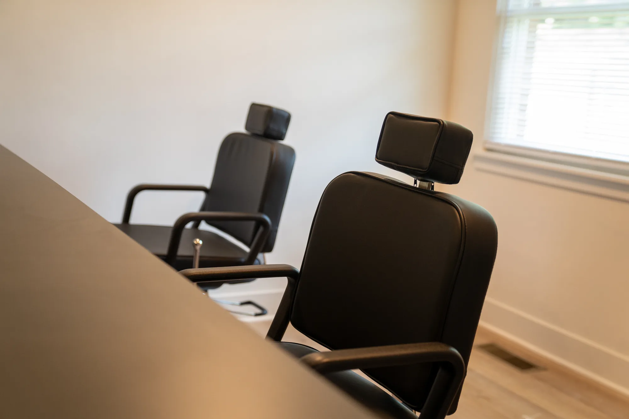 Two black barber chairs beside a sunlit window on the academy clinic floor.