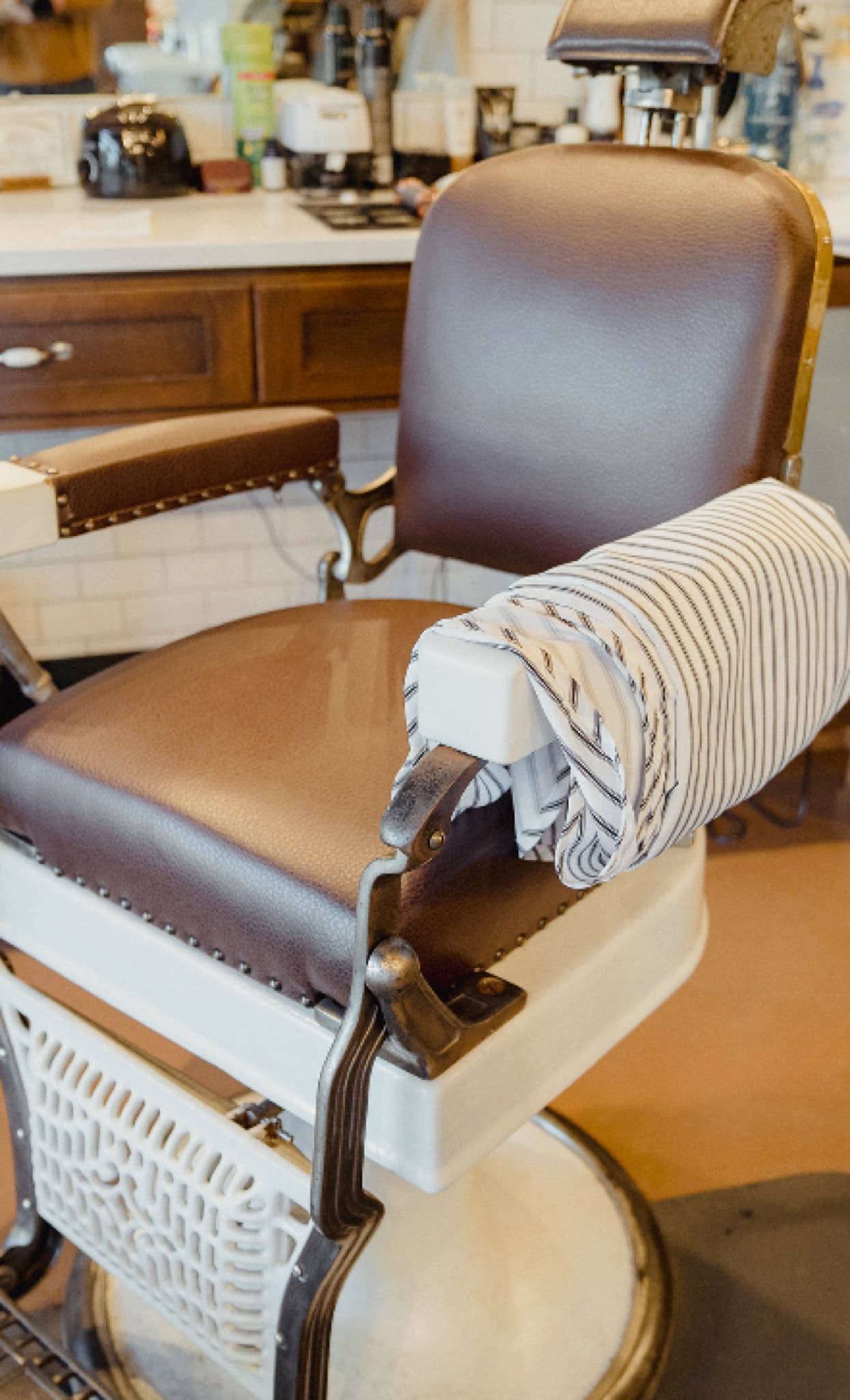 A vintage barbershop chair with a striped barber's apron draped over the armrest.